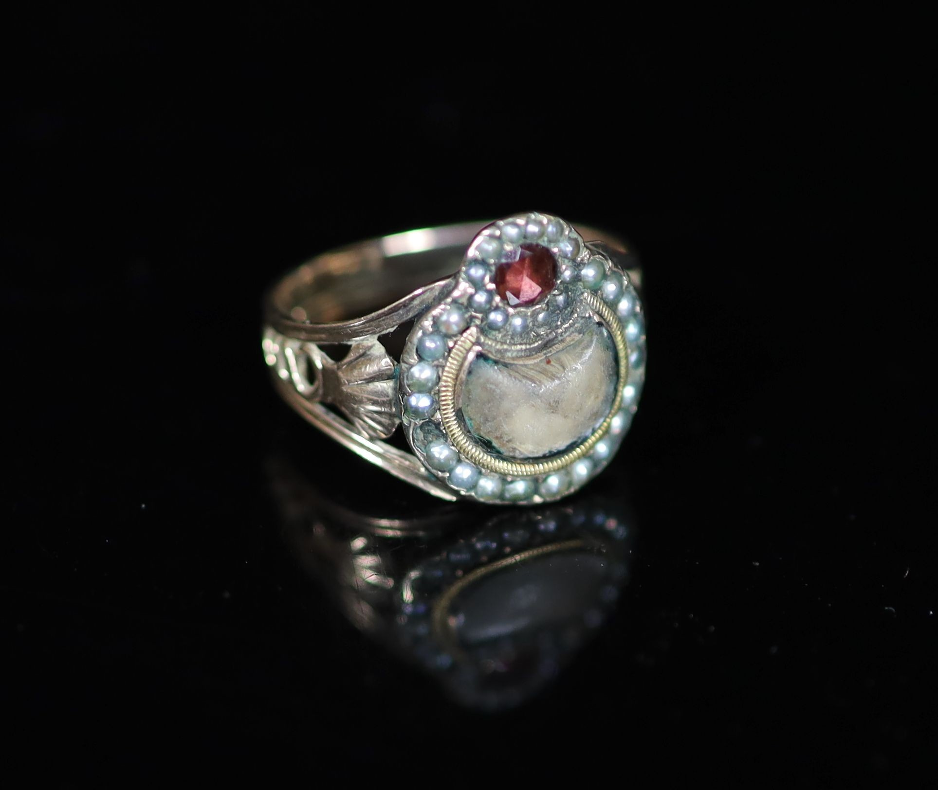 A 19th century gold, seed pearl and garnet? set mourning ring, with plaited hair beneath a glazed panel